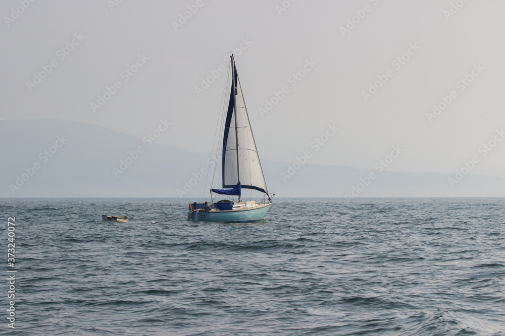 Sailing boat with a white sail on the ocean in summer. Blue sky and blue sea