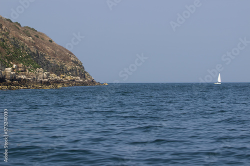 Summer day on the water at puffin Island in the Menai straits, Anglesey. Small sailing boat next to a rocky cliff.
