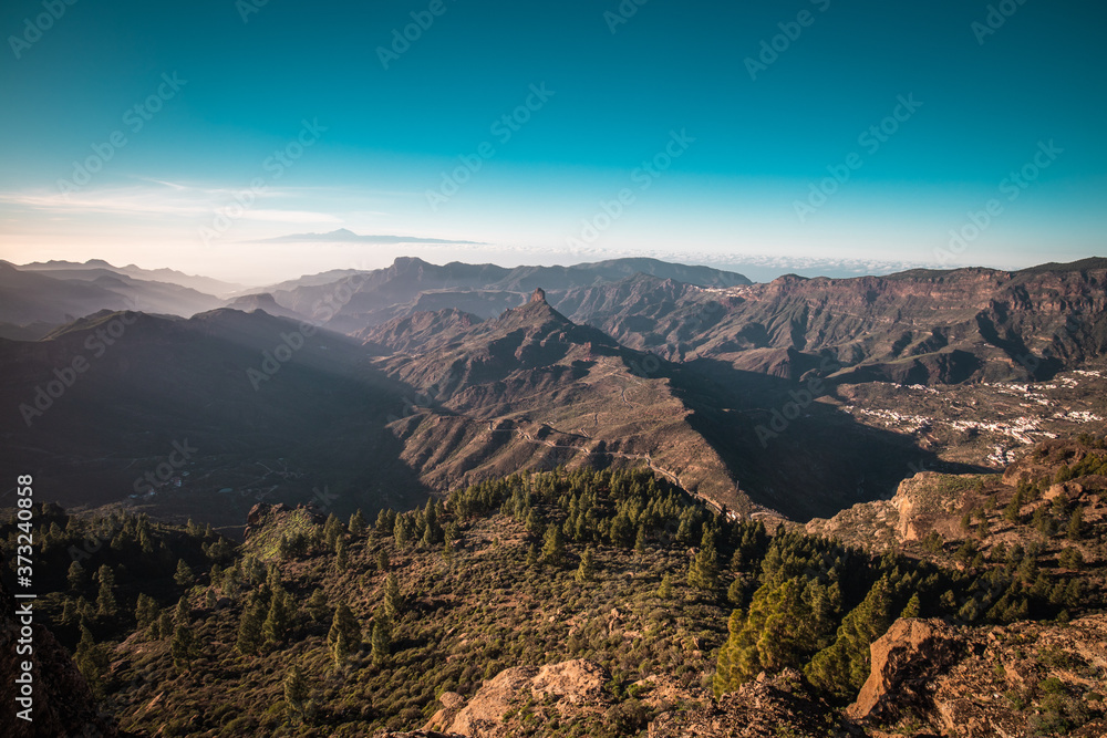 A panorama view of a sunset over the Roque Nublo in Gran Canaria, Spain. Tenerife is visible in the background.