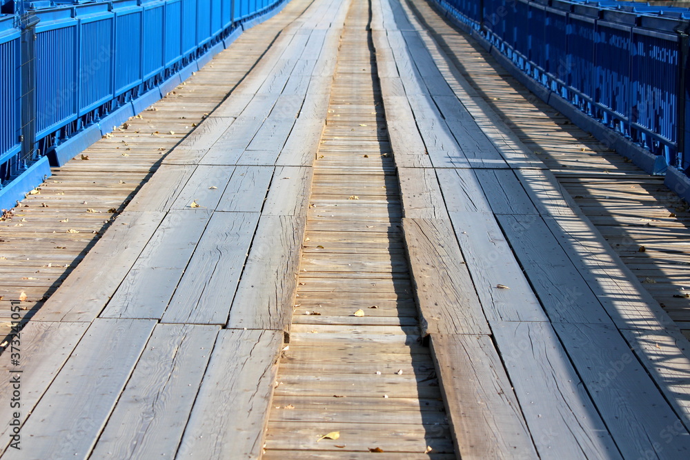 Long partially renovated wavey old wooden bridge with new blue metal frame on each side and strong support on warm sunny autumn day