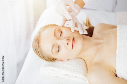 Beautician doctor doing beauty procedure with syringe to caucasian female face in synny room. Cosmetic medicine and surgery, beauty injections concept