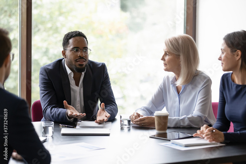 Confident african trainer or coach giving recomendations to diverse group of clients, dark-skinned boss holding a meeting with staff, multiethnic team listening to leader explaining his point of view