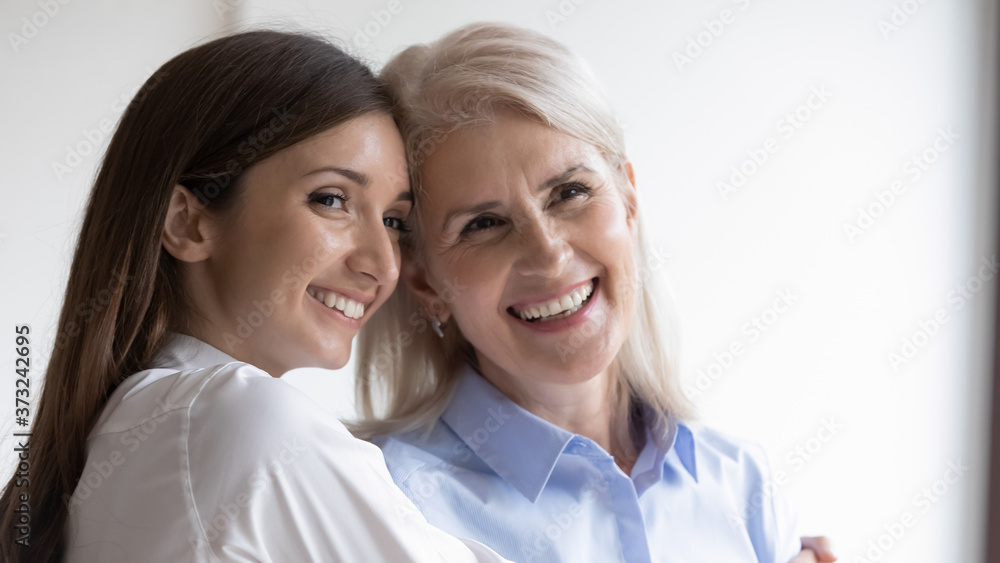 Head shot portrait of beautiful happy older mother and adult daughter embracing and leaning heads to each other looking aside. Warm family relations, enjoying spending time together. Copy space Head shot portrait of beautiful happy older mother and adult daughter embracing and leaning heads to each other looking aside. Warm family relations, enjoying spending time together. Copy space