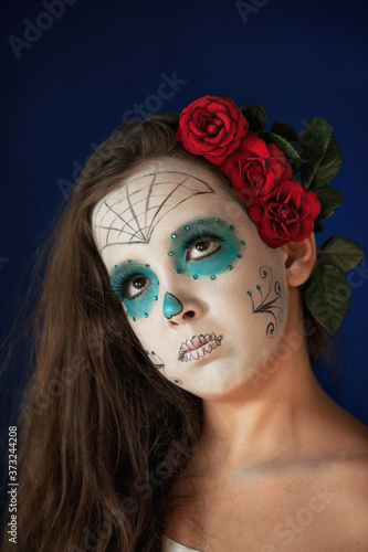 Halloween make up sugar skull beautiful model with perfect hairstyle, red roses in hair. Santa Muerte concept.