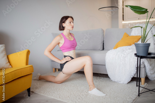 Fitness woman in athletic workout clothes training indoor home, uses stretching for trainer online. Interior room modern