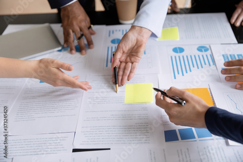 Close up of diverse businesspeople group discussing charts and graphs on meeting, multiethnic team of corporate managers or employees analyzing information materials hardcopy in office together