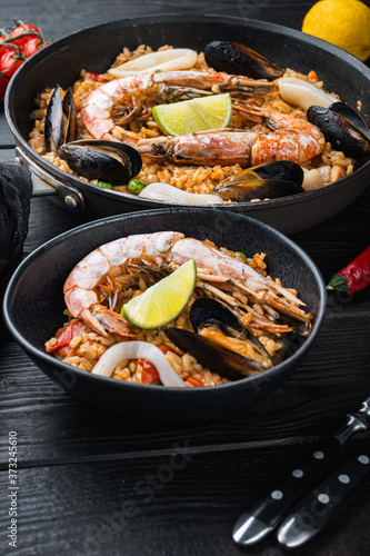 Typical spanish seafood paella in traditional pan and black bowl on black wooden background