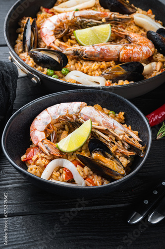 Typical spanish seafood paella in traditional pan and black bowl on black wooden background