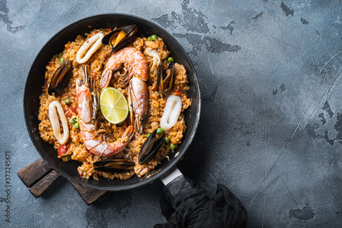 Paella with seafood, prawns, musselsm chicken and rice in pan on grey textured background, top view with space for text