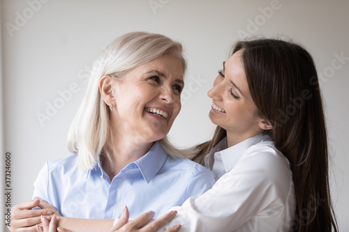 Beautiful millennial woman holding her aged happy mother in arms with affection and love, positive senior lady and her grown-up daughter embracing and looking in each other eyes with tender smiles
