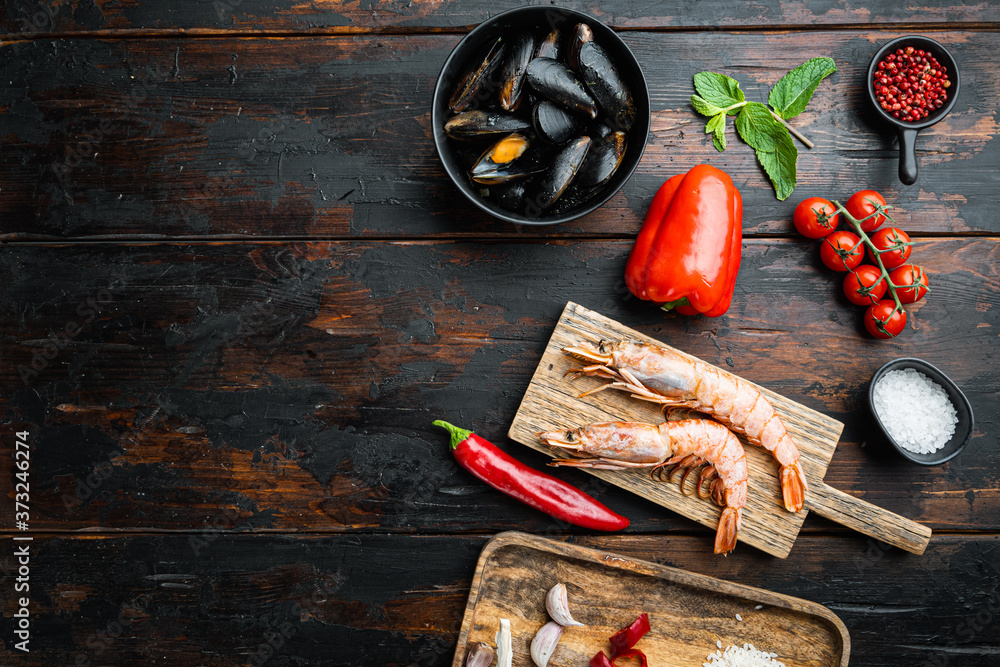 Typical seafood paella ingredients with rice, mussel, prawns and cuttlefish over dark rustic wooden background, flat lay with copy space