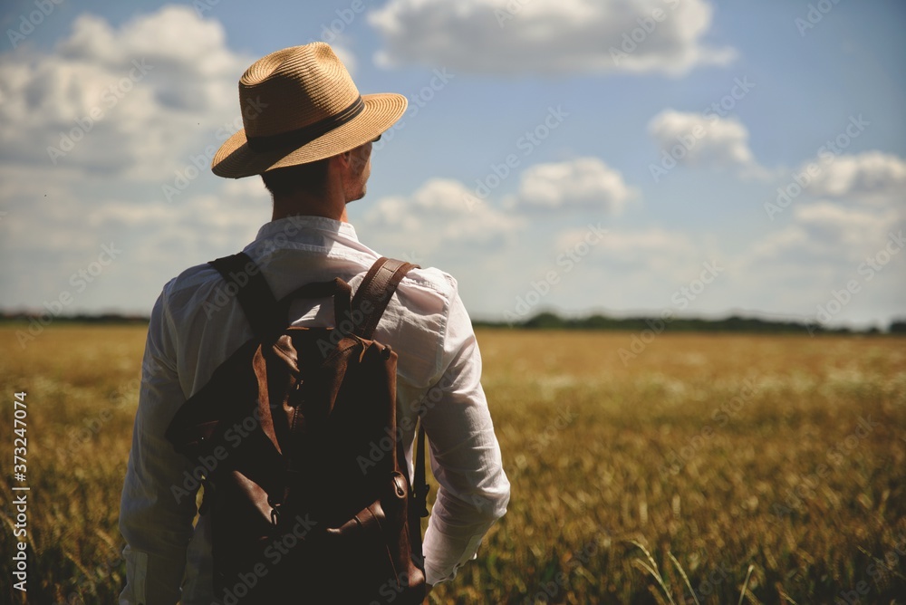 Tourist man with backpack goes in field landscape back view. Hiker hipster male enjoy adventure walks on countryside path. Adventure Trip in Natural landscape.