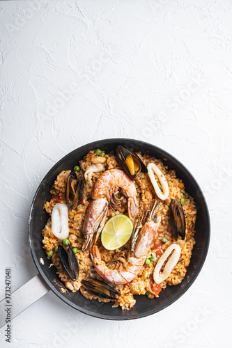 Seafood and chicken paella with rice, mussles, shrimps,chicken, tomatoes and wine in pan on white textured background, flat lay with copy space