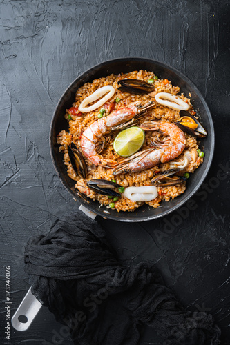 Valenciana paella with king prawns, mussels and squid on black background, flat lay