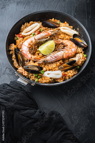 Paella traditional spanish dish served in frying pan, on black textured surface