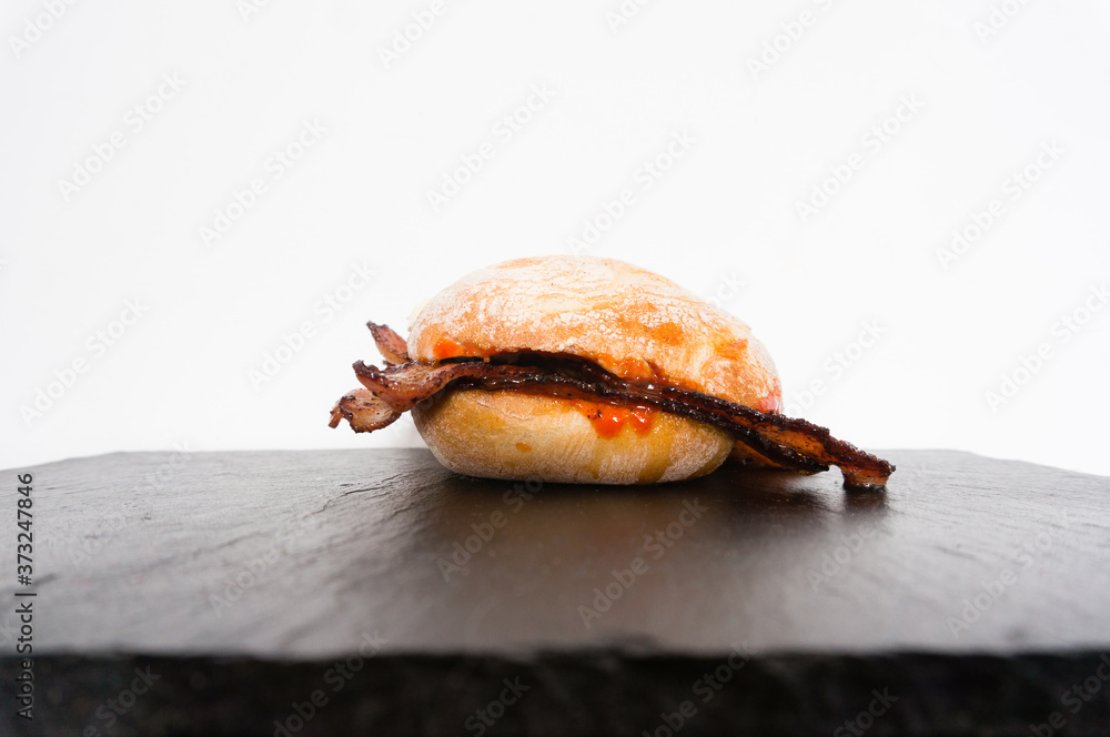 Isolated classic British bacon sandwich served on a black slate and presented against a white background Isolated classic British bacon sandwich served on a black slate and presented against a white background