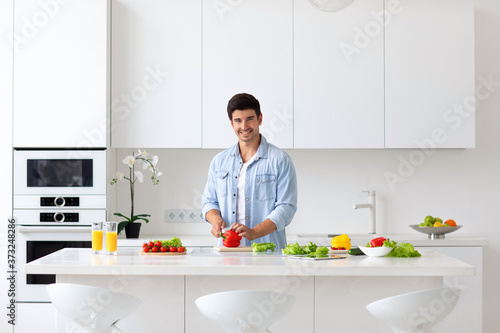 Millennial man stand at modern kitchen table cooking tasty and healthy food in kitchen at home.