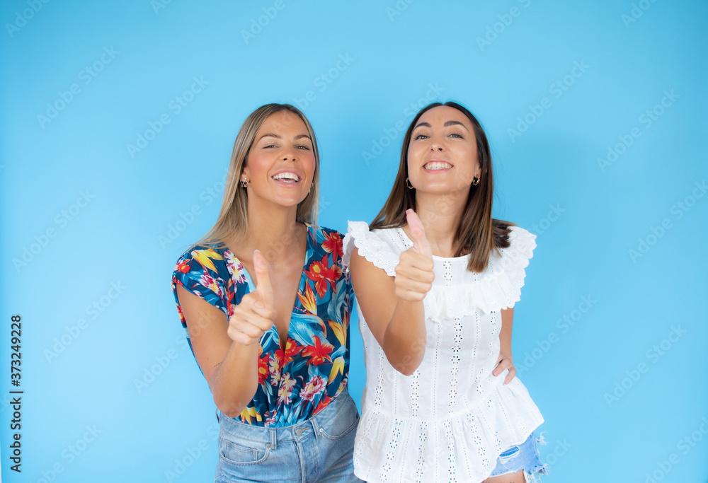 Two friends with summer clothes making finger up gesture Two friends with summer clothes making finger up gesture