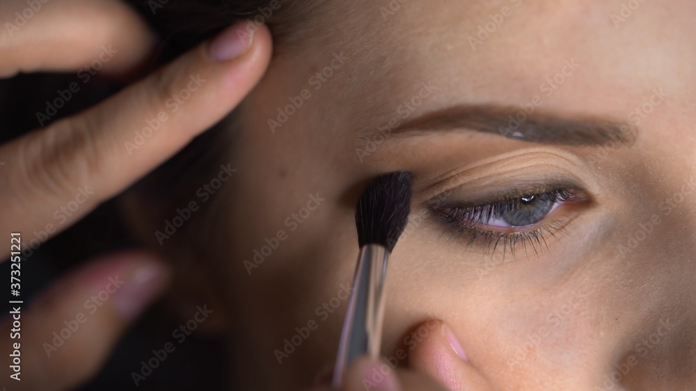 Macro shot of Professional Makeup for beautiful and gorgeous woman sitting at the Studio. Make up Artist applies blush with brush on eyelid