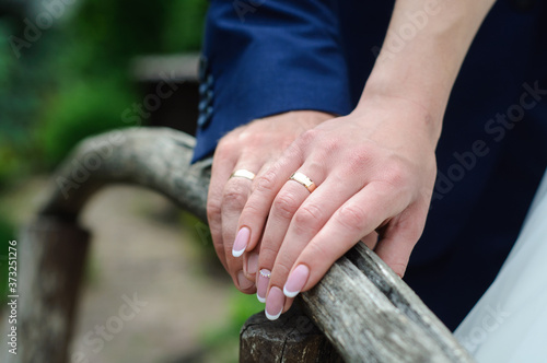The bride's hand rests on the groom's hand. Gold wedding rings