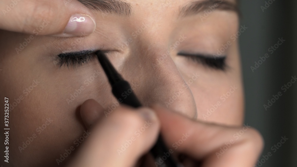 Makeup artist making professional make-up for young woman in beauty studio. Make up Artist applies black eyeliner to eyelid
