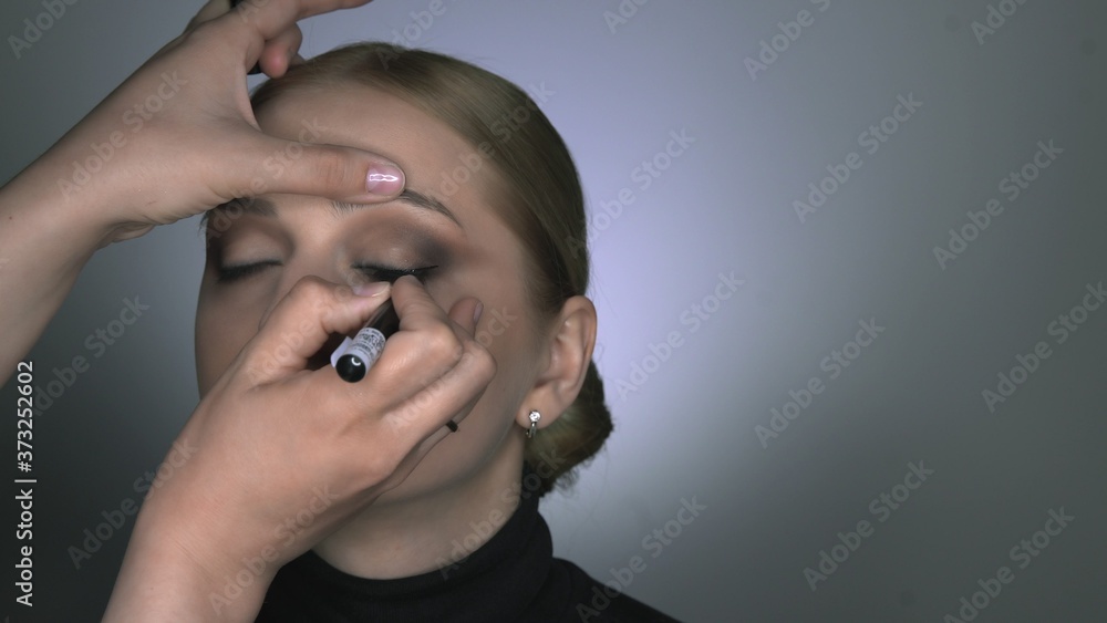 Makeup artist making professional make-up for young woman in beauty studio. Make up Artist draws arrows over eye, eyeliner Makeup artist making professional make-up for young woman in beauty studio. Make up Artist draws arrows over eye, eyeliner