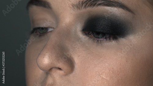 Macro shot of makeup artist making professional make-up for young woman in beauty studio. Make up Artist makes the makeup smokey eyes of a black shade with special brush of a beautiful model