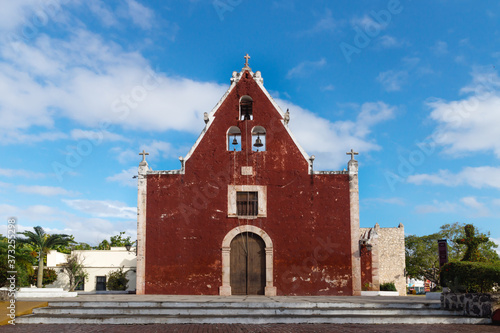 Entrance of the red colonial church Itzimna in a park with trees, Merida, Yucatan, Mexico photo