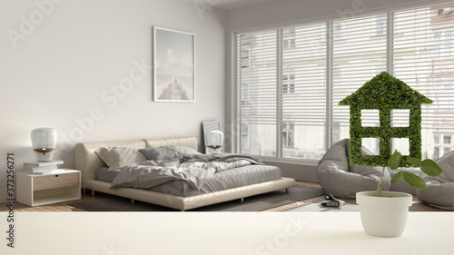 White table top or shelf with green plant in pot shaped like house, modern bedroom with double bed background, interior design, real estate, eco architecture concept idea