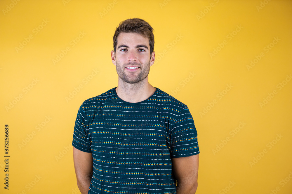 Young handsome man wearing casual blue t-shirt standing over yellow background with a happy and cool smile on face. Lucky person. Young handsome man wearing casual blue t-shirt standing over yellow background with a happy and cool smile on face. Lucky person.