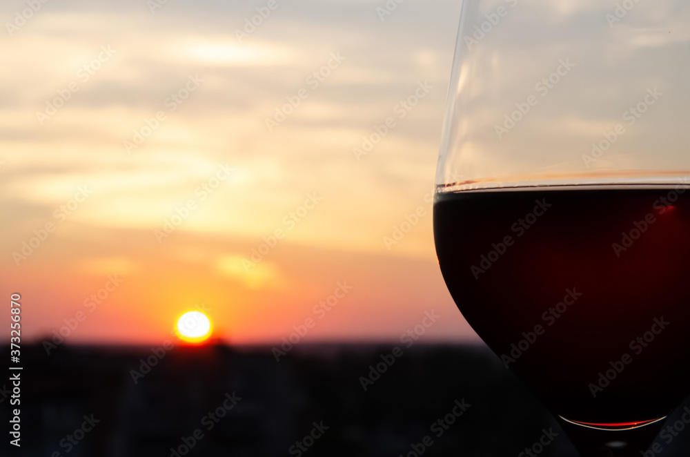 Close-up glass with red wine on a blurred background with copy space. Part of a wine glass on a sunset sky background. Sunset. Beautiful sunset with a glass of wine in the foreground.