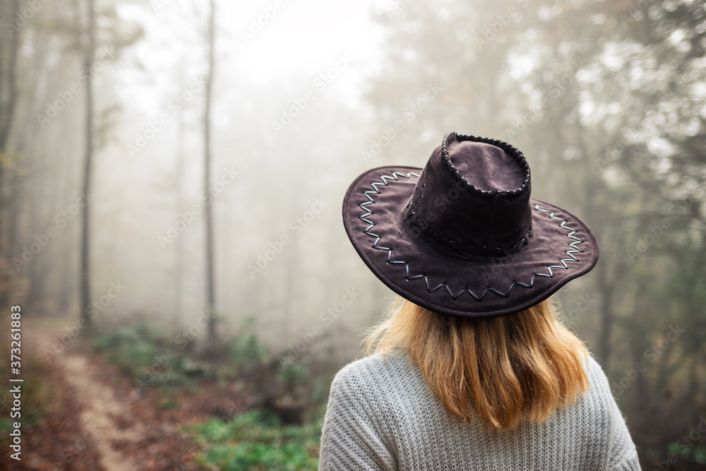 Woman tourist with hat looking at fog in forest during hike