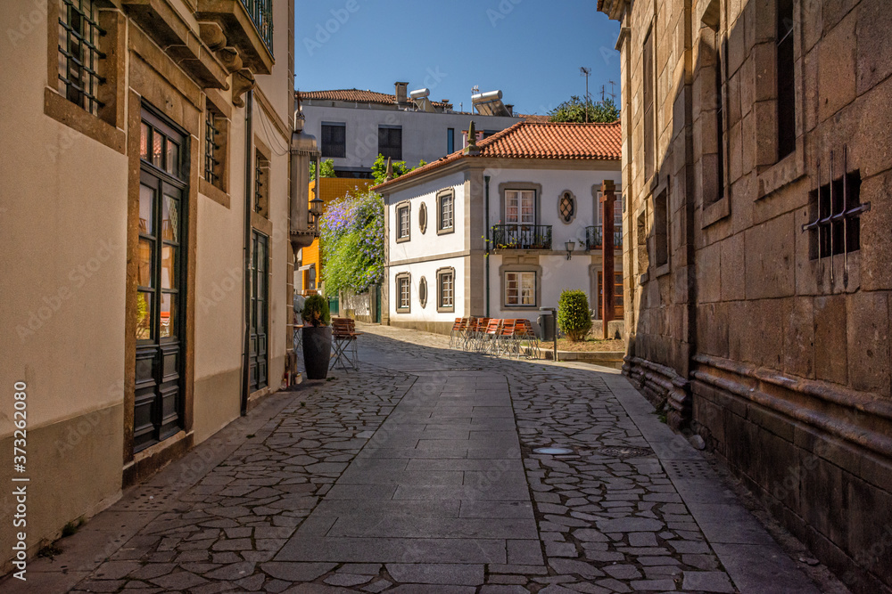 Shadowed Cobblestone Alley With Old Wall And Sunlit Building In Background, Braga, Portugal 