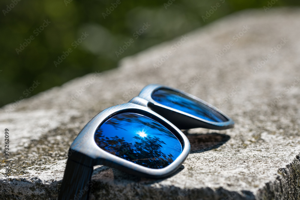 Classic sunglasses model with blue lenses and blue frame in a sunny day closeup . Selective focus