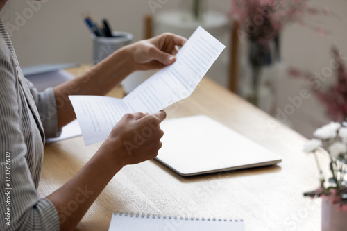 Close up young woman holding paper letter with good news, getting banking loan approval. Millennial businesswoman received correspondence, reading fashion show or special event invitation indoors. photo