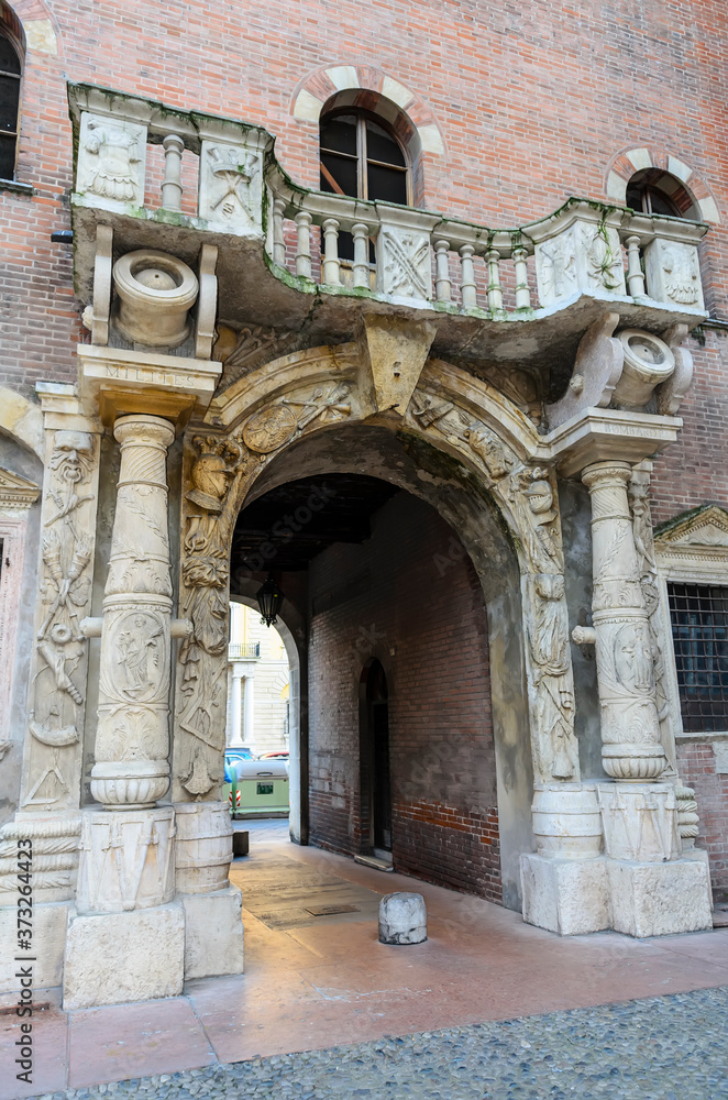 Arched gate decorated with a balcony, columns in the form of cannons, bas-reliefs in the form of knight armor and coats of arms in the courtyard of the Palace of Cansignorio. Verona, Italy