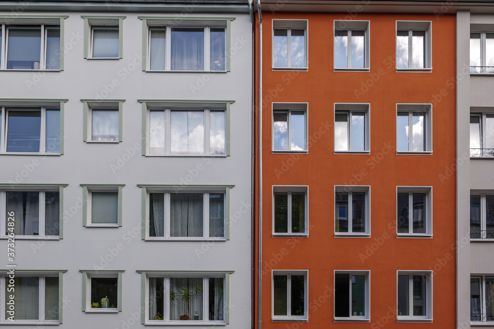 Outdoor sunny exterior front view, typical facade of modern residence or apartment in city of Europe with various rectangular windows, white and red wall.