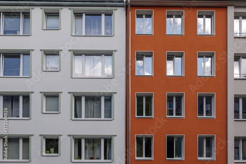 Outdoor sunny exterior front view, typical facade of modern residence or apartment in city of Europe with various rectangular windows, white and red wall.