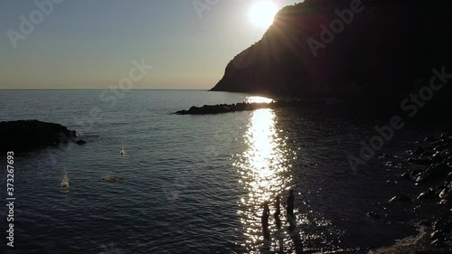 three boys in the beach playing  throwing stones into the sea with the sun reflected in the water
