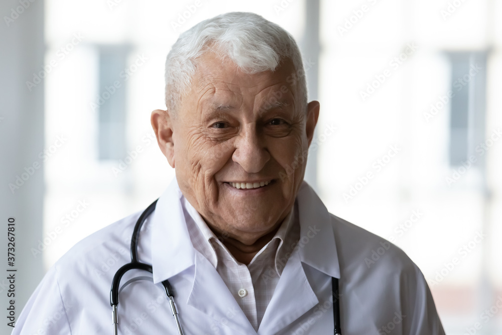 Head shot close up smiling pleasant old qualified head doctor, wearing white medical coat with stethoscope. Portrait of skilled experienced trustful elderly 70s general practitioner therapist surgeon. Head shot close up smiling pleasant old qualified head doctor, wearing white medical coat with stethoscope. Portrait of skilled experienced trustful elderly 70s general practitioner therapist surgeon.
