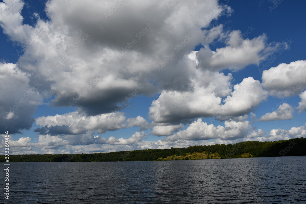 A picturesque view of a large river with green banks. Beautiful clouds are reflected in the water.
