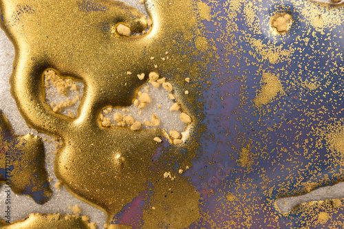 Piles of gold sequins on blue liquid ink background. Abstract pattern.