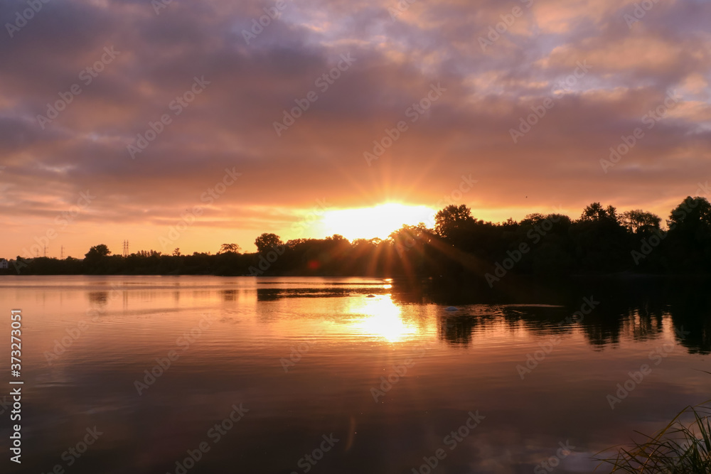 Symmetry of the sky in a lake at sunrise. Clouds reflecting on the water. Holiday landscape by the sea. Quiet relaxing scene with a beautiful colorful sky and rays of sun. 