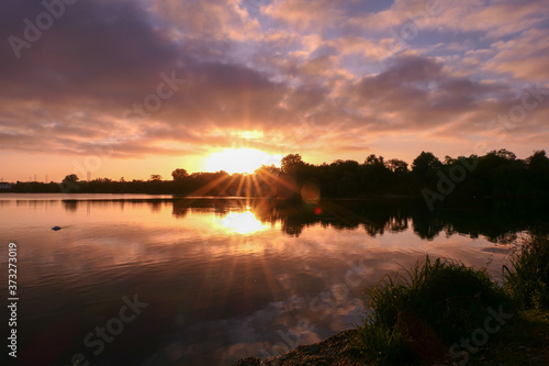 Symmetry of the sky in a lake at sunrise. Clouds reflecting on the water. Holiday landscape by the sea. Quiet relaxing scene with a beautiful colorful sky and rays of sun. 