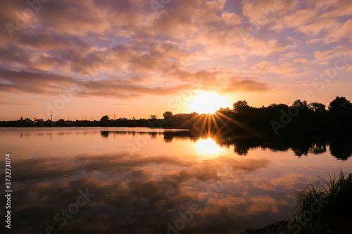 Symmetry of the sky in a lake at sunrise. Clouds reflecting on the water. Holiday landscape by the sea. Quiet relaxing scene with a beautiful colorful sky and rays of sun. 