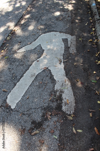 Walking sign on asphalt missing head.