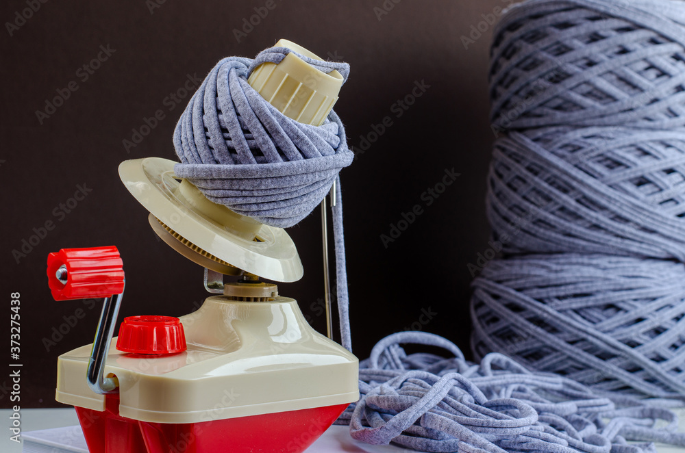 hand plastic wool winder at work, gray yarn balls, brown background. prepair for knitting, crochet. handmade concept - obrazy, fototapety, plakaty 