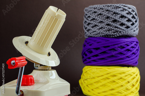 Fotografía hand plastic wool winder, yellow, purple, gray yarn balls, brown background