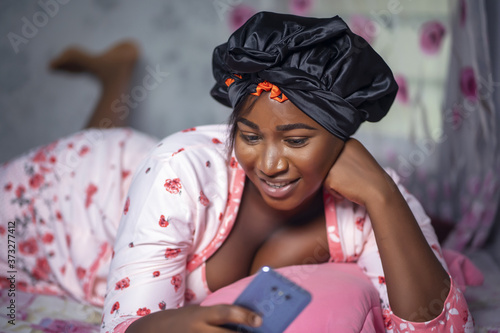 Portrait of a young African American female in a satin bonnet using her phone on her bed photo