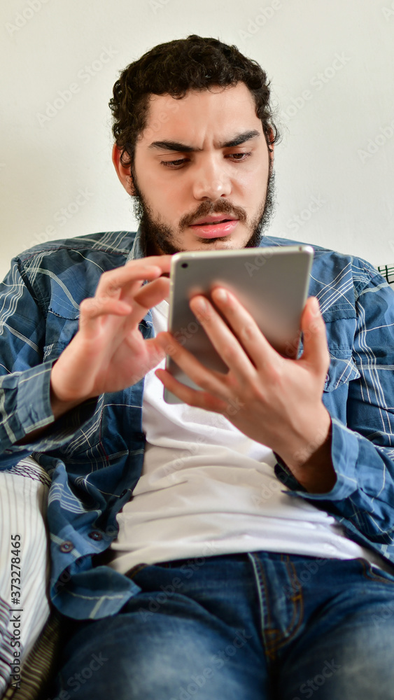 Young man using a tablet sitting on the couch in the living room at home Young man using a tablet sitting on the couch in the living room at home